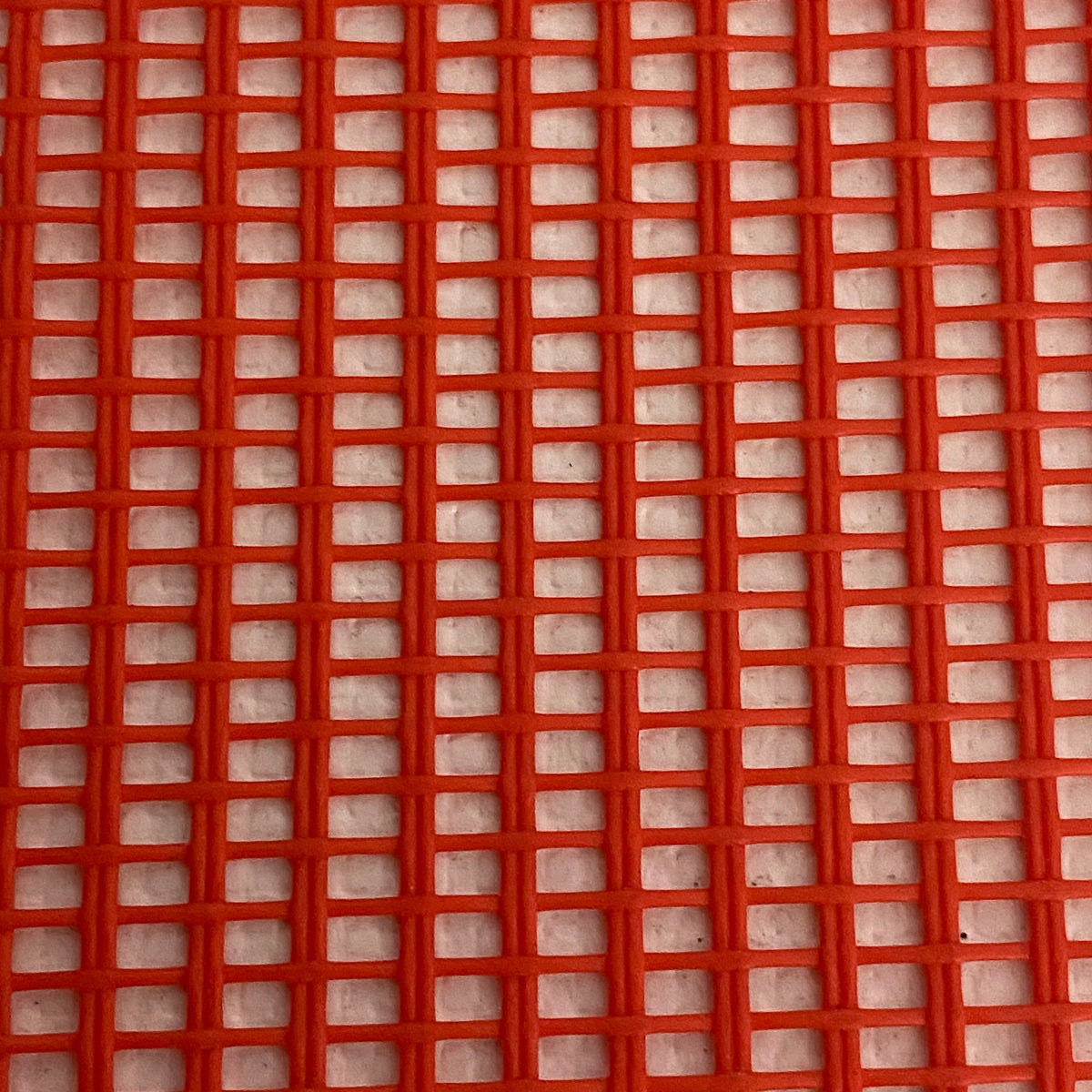 Close-up view of a heavy-duty red mesh tarp made of UV-resistant polyester, featuring a pattern of square openings.
