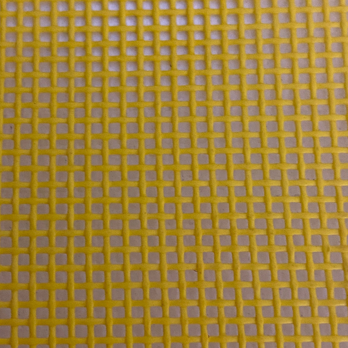 Close-up view of a heavy-duty yellow mesh tarp made of UV-resistant polyester, featuring a pattern of square openings.