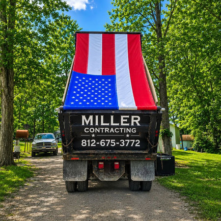 Truck with American flag design on the back, parked on a dirt road with trees in the background.