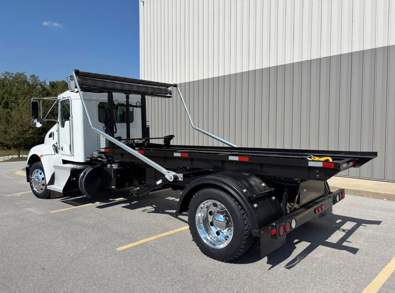 White rolloff truck with a black bed parked in front of a building